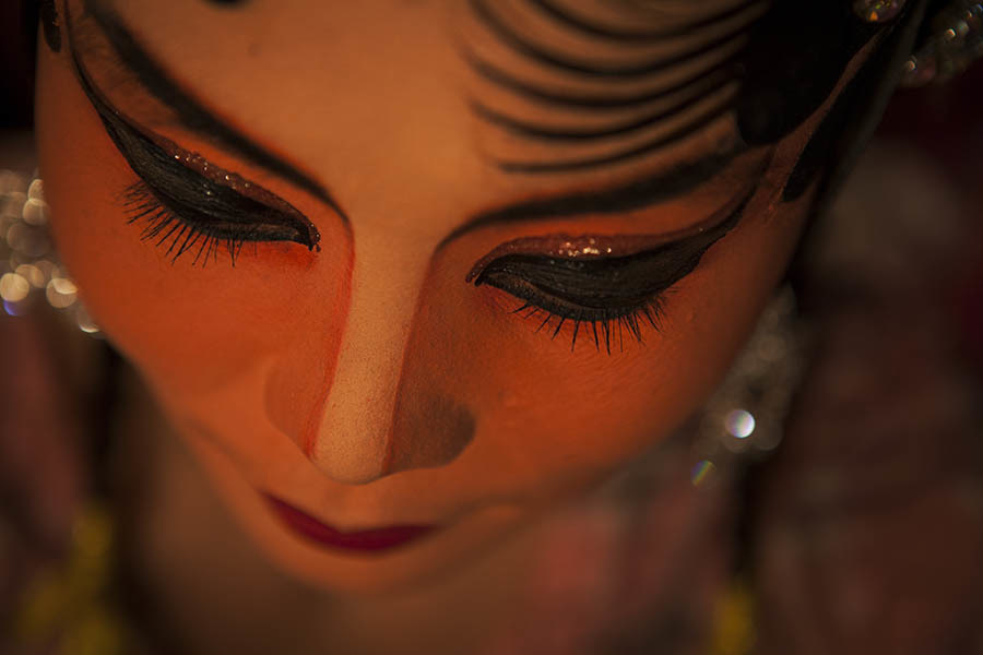 A detail shot of a Chinese opera performer just before she goes on stage. Chinese opera is performed in Thailand by itinerant groups of players, most of whom are from the northeastern region of Thailand known as Isan. It is characterised by its lavish costumes, the falsetto delivery of its actors and the highly stylised presentation of its set-piece stories which are drawn from Chinese folklore. Though the operas are performed in Chinese most of the actors don't understand Chinese and simply learn their parts by rote. Chinese opera is colourful reminder of the importance of Thailand's ethnic Chinese population, and of how Chinese culture has become an integral part of Thailand's cultural identity. Though the Chinese opera is appreciated by an ageing, and dwindling, population of Chinese speakers, the performers explain that audience sizes is of little importance since they essentially performing for the gods. The shows are usually sponsored by the local community, are free for all to attend and usually last between two and three days.